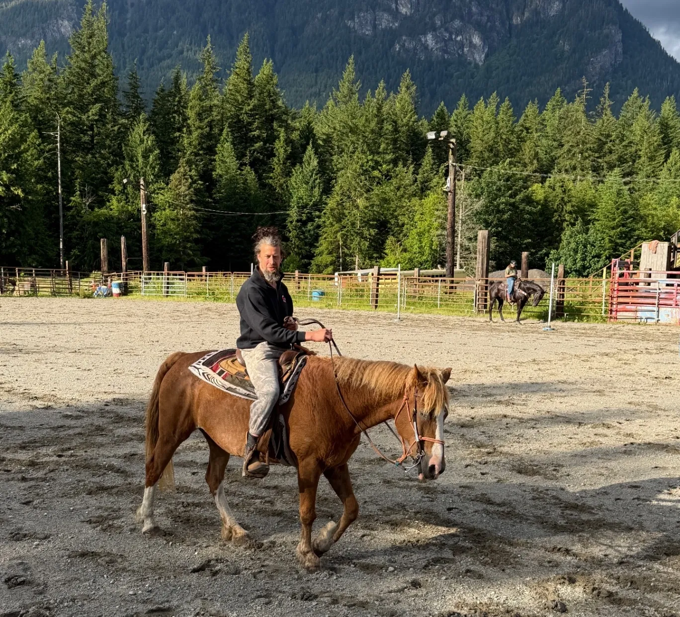 A resident riding horseback in the arena with mountains behind
